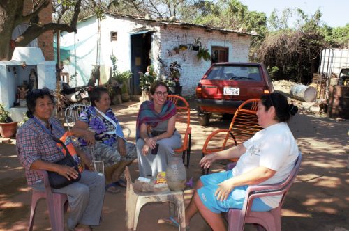 A young volunteer sitting and talking with local women outside a house in Bañado Tacumbú, Paraguay