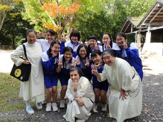 Sisters in white habits with smiling Japanese schoolgirls in uniform making the peace sign