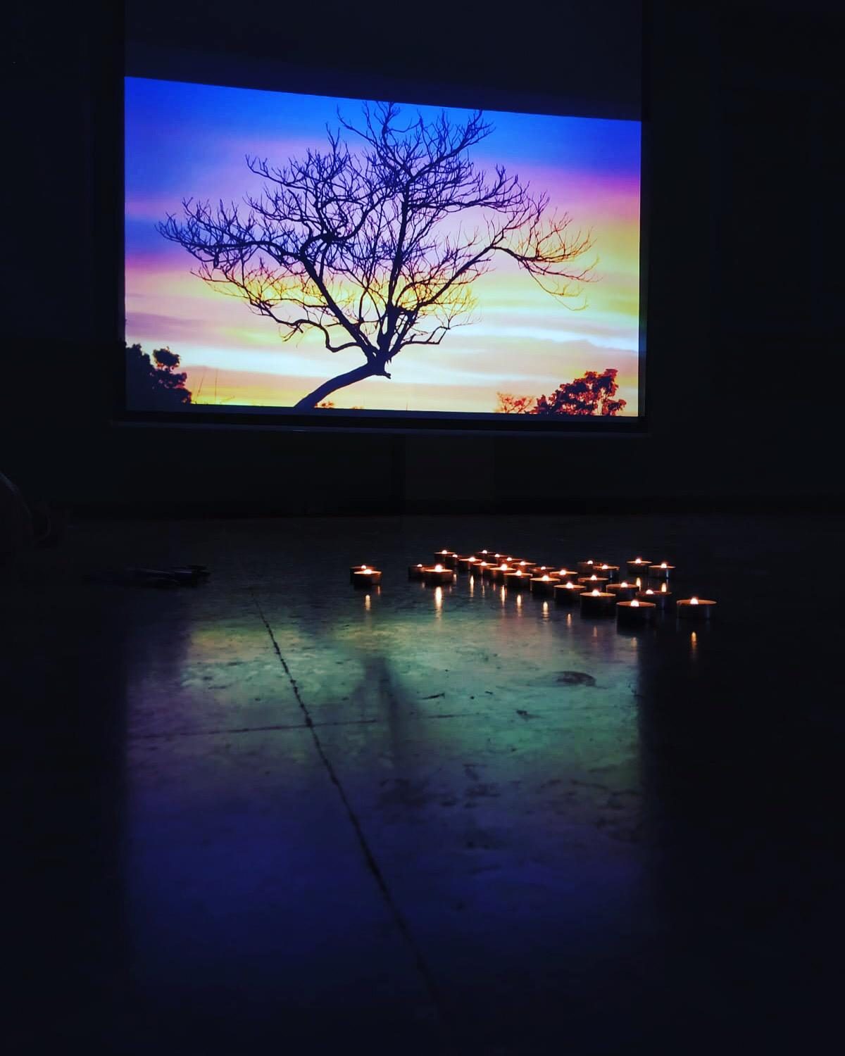 Tealight candles on the floor in front of a screen showing a bare tree at sunset, set up for the MJD Spain prayer
