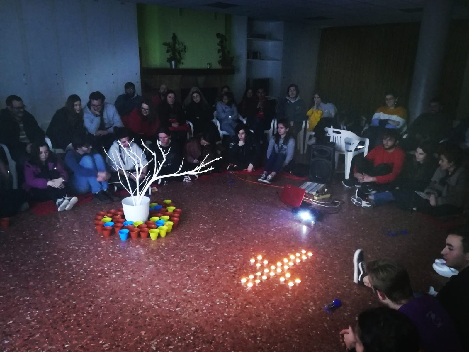 Young people seated in a circle around a white branch tree, flowerpots and candles during the prayer