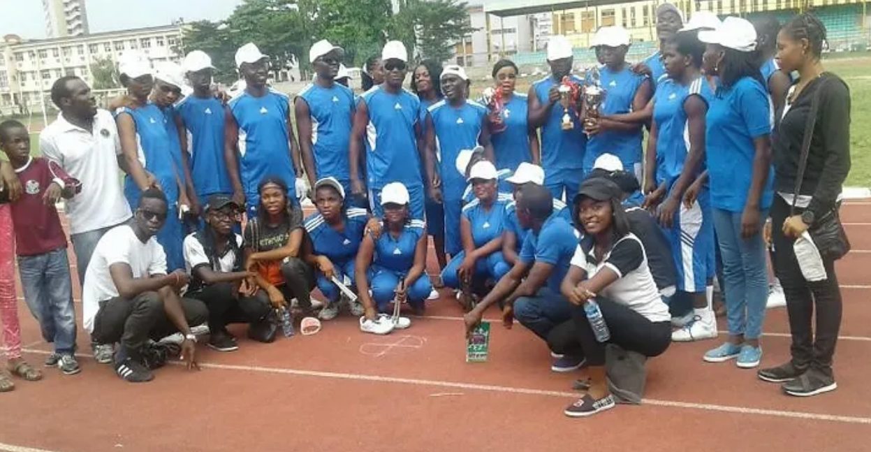 Young Dominicans in Nigeria pose with athletes in blue uniforms holding trophies on a running track