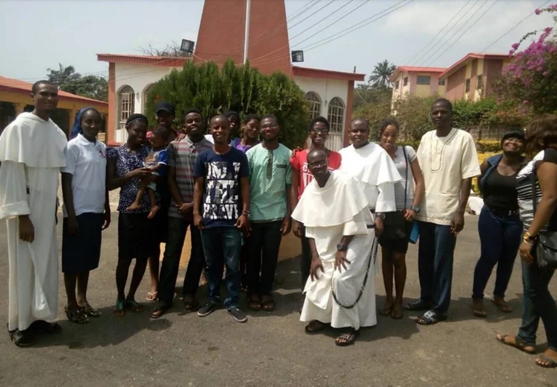 Dominican friars in white habits with young people and a child outside a church in Nigeria